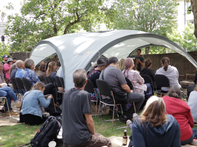 A number of people seated at a workshop outside and under a white gazebo